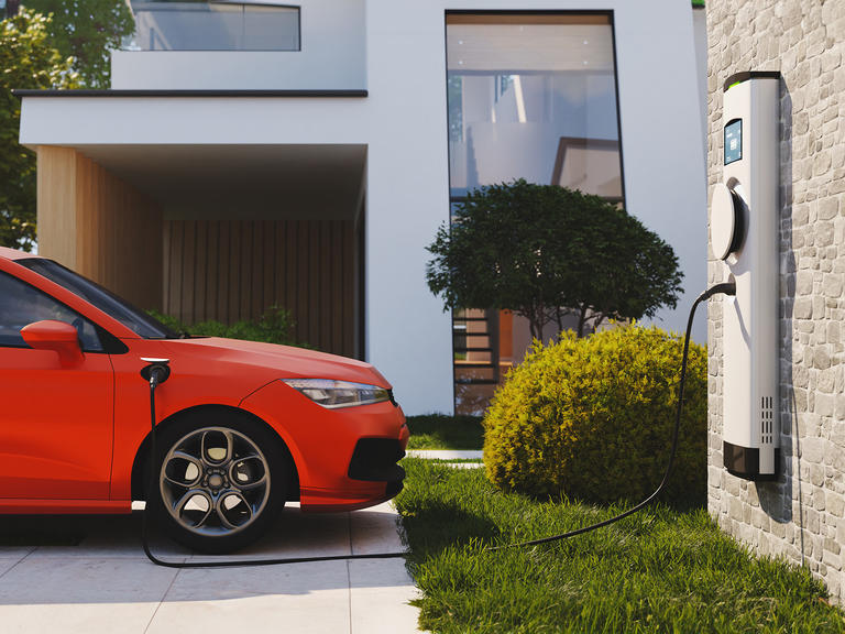 Red EV plugged into a charger attached to house