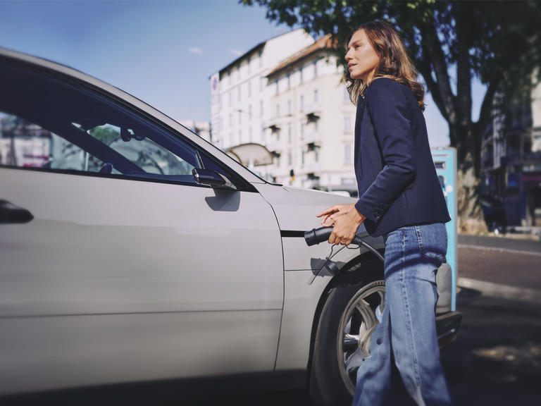 A woman plugs in her electric car at an EV charge point.
