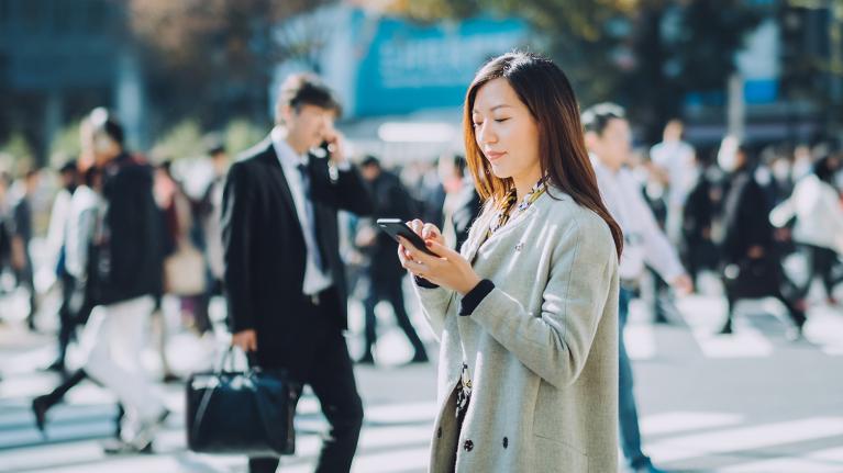 街なかでスマートフォンを使いながら正確なジオコーディングで高精度位置情報を取得する女性