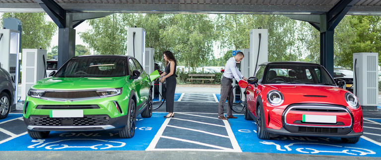 Two drivers recharge their electric vehicles at a charging station.