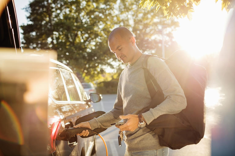 Man charging vehicle looking at phone