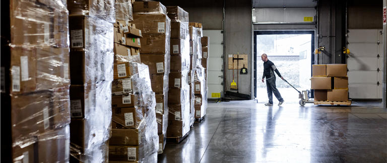 A man pulling a hand pallet truck in a busy warehouse.