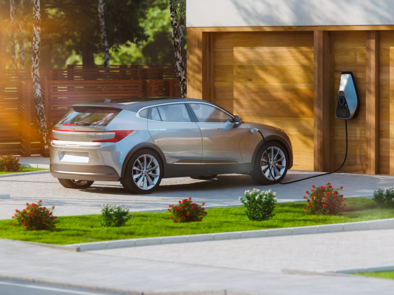 A car parked in the driveway of a house, plugged in at a home chargepoint.