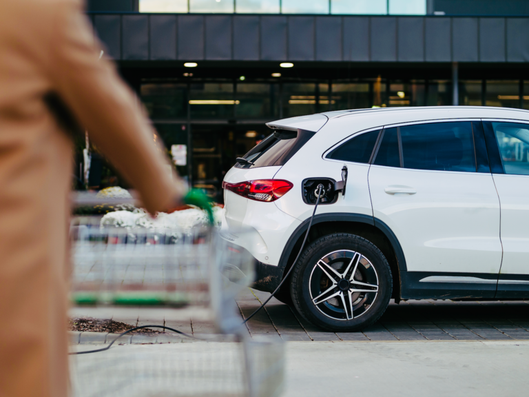 A person pushes their shopping cart toward their parked electric vehicle.