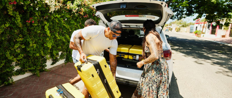 Three friends pack their electric car's trunk on a sunny day.