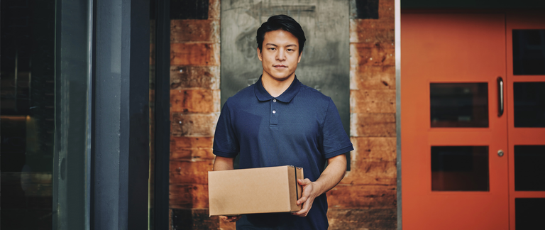 A delivery driver holds a package, looking straight to camera.